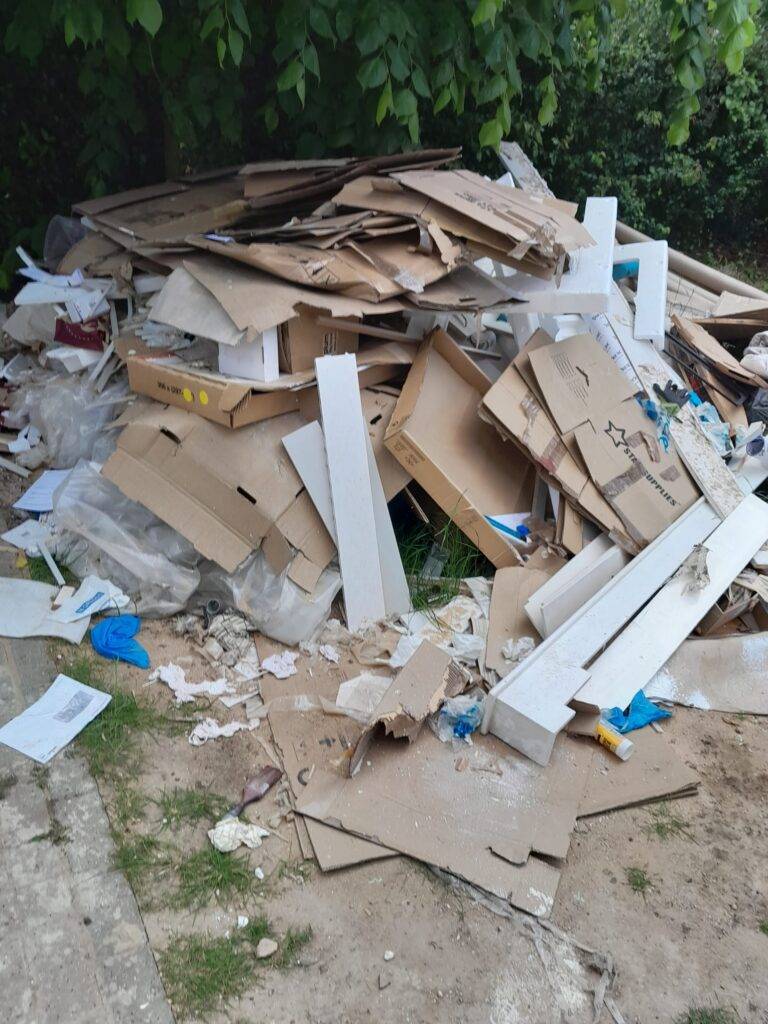A pile of rubbish on some land in front of a tree where people had been Fly-Tipping and a fly-tipping clearance service is required. The rubbish removal service is near Essex and London postcodes.