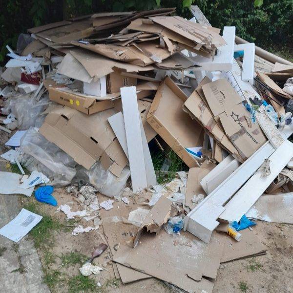 A pile of rubbish on some land in front of a tree where people had been Fly-Tipping and a fly-tipping clearance service is required. The rubbish removal service is near Essex and London postcodes.
